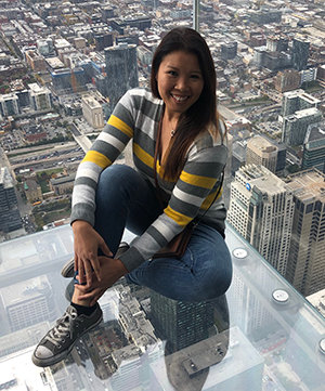 Photo of Loribeth sitting in a glass building with the view of a city behind her