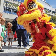 In a large outdoor crowd, two young kids stand before a performer operating a large red and yellow dragon puppet
