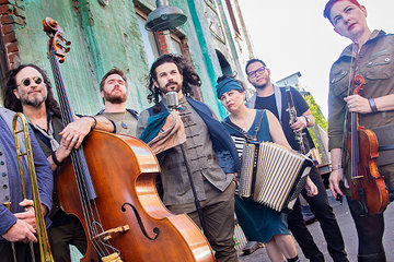 Members of the band Mostly Kosher standing outside on a city street holding musical instruments