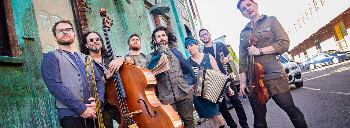Members of the band Mostly Kosher standing outside on a city street holding musical instruments