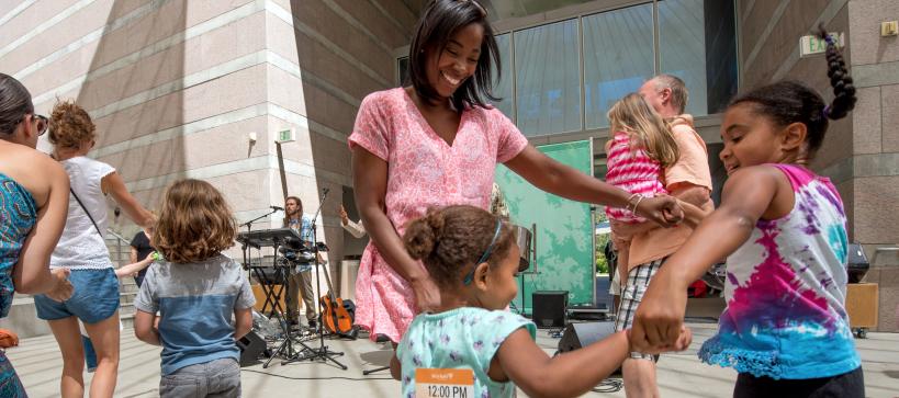 Mother and two daughters holding hands and dancing in a circle to a live band in the outdoor amphitheater.