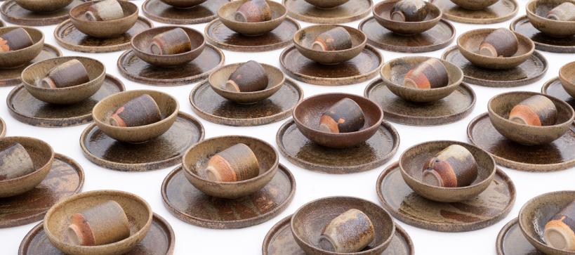 A pattern of a plate, bowl, and cup stacked and put in rows. The dishes are made of brown earthy pottery.
