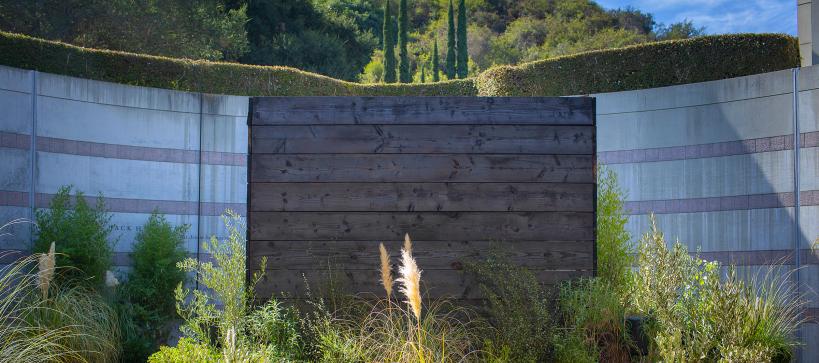 A structure made of dark burnt web planks in the middle of green plants in a courtyard