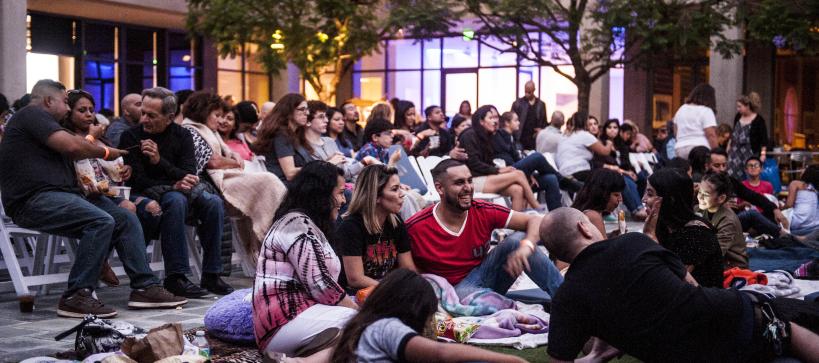 A large group of people sit in a courtyard laughing and talking.