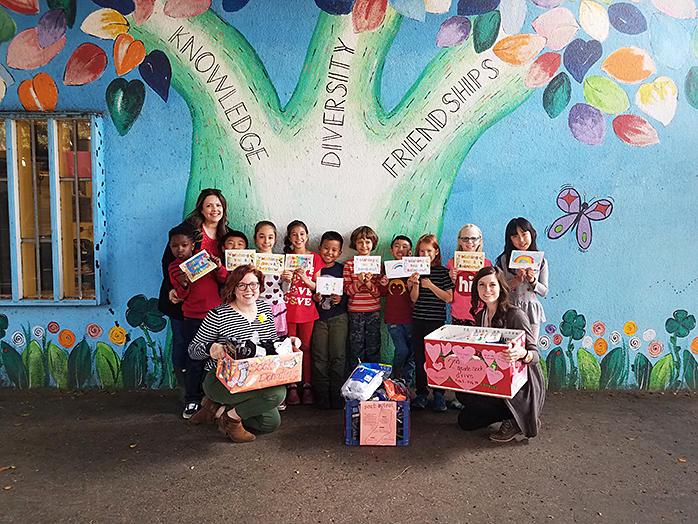 Class of young students holding hand-made cards and boxes in front of a mural of a tree