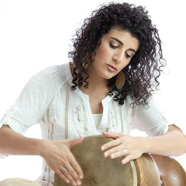 Headshot of the musician Galeet dressed in white and playing a drum with her hands.