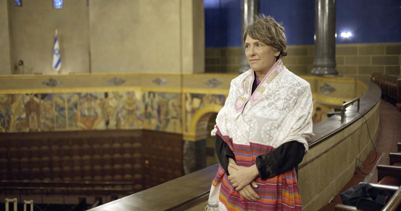 A person wearing a prayer shawl stands with hands clasped