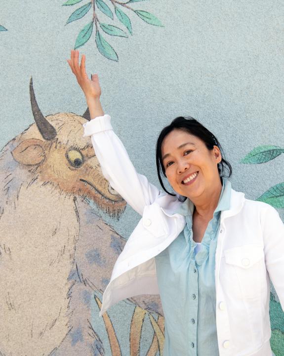 A woman poses next to a mural of a wild creature.