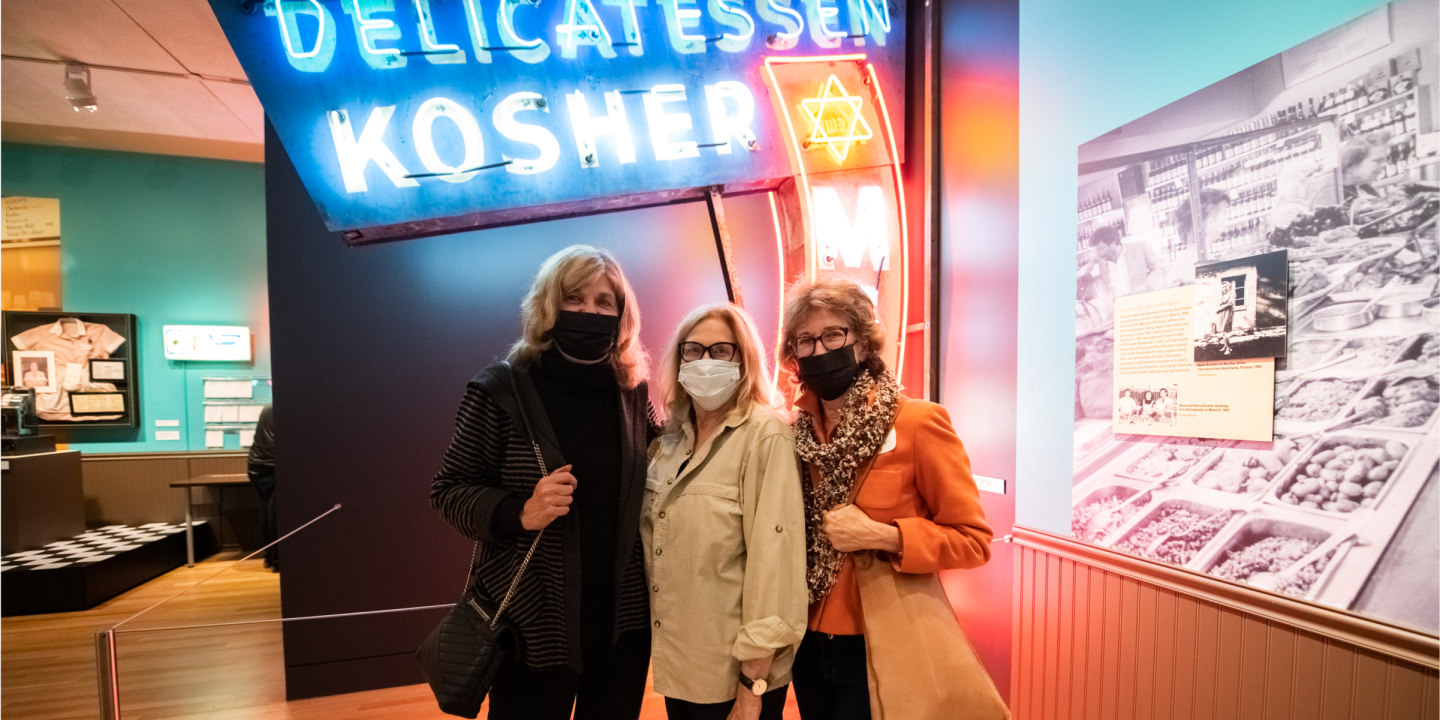 3 women in front of a neon sign that says Delicatessen Kosher