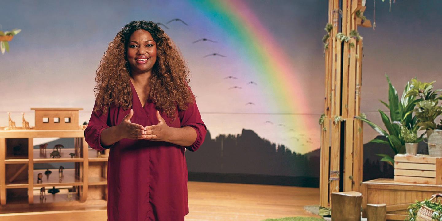 Educator smiling and standing in Noah's Ark exhibition with rainbow in the background 