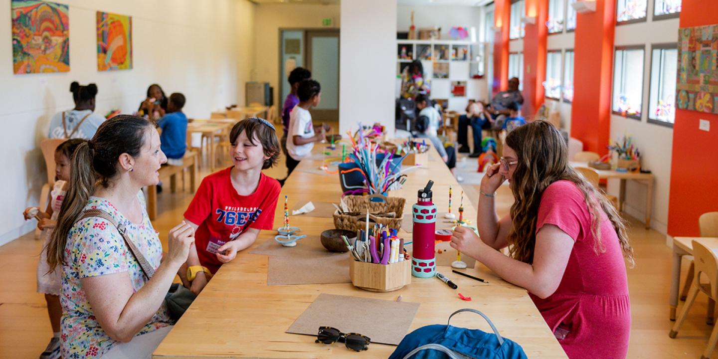 Art studio filled with young people and adults interacting around tables