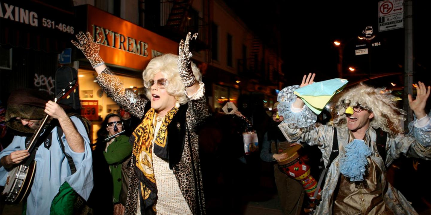Amichai Lau-Lavie dressed as his drag character Rebbetzin Hadassah Gross dancing down a street at night with a crowd of musicians and party-goers.