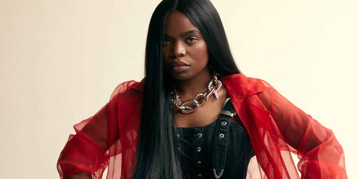 The artist Vagabon, dressed in red and black, looking directly into the camera.