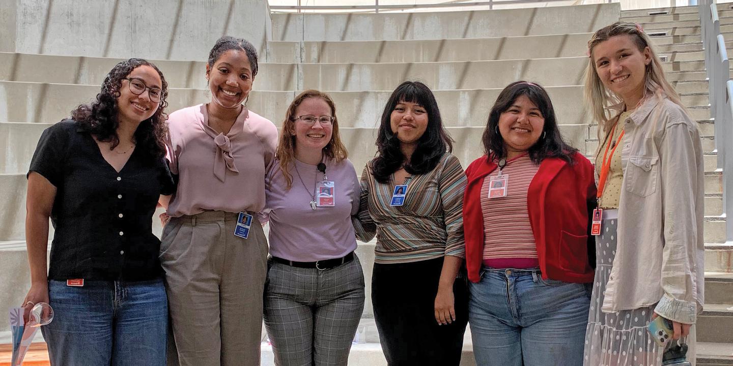 Six young women standing together smiling for a photo in an amphitheater.