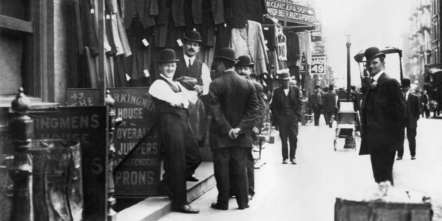 Black and white photograph showing men in suits and bowler hats standing on a street in a city garment district.