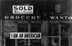 a sign that says 'sold' above a grocery store sign; below the grocery sign is another that says 'I am an American'