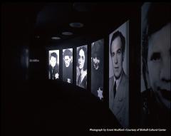 dark room with backlit photos of people with Jewish stars on their clothing