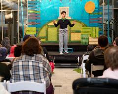 A person is on a stage telling a story to a group of adults and children