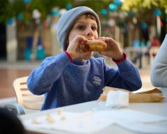 Photo of a young child wearing a blue sweater and beanie eating a jelly donut