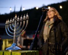 A hanukkiah sits outside in front of a woman speaking into a microphone