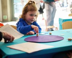 A young child plays with a dreidel on a purple mat on a table