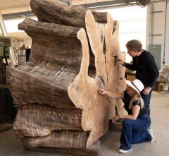 Artists Tiffany Shlain and Ken Goldberg point at different areas of a large tree stump that has been cut in a cross section and turned on its side to display the natural occurring rings.