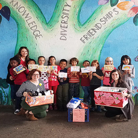 students and teachers holding posters and boxes in front of a mural of a tree