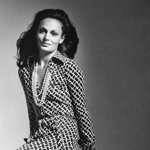 Black and white portrait of Diane von Furstenberg posing in her famous wrap dress smiling at the camera.
