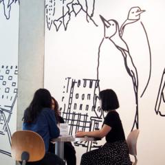 black and whilte drawings on wall with 3 people seated at a small table in front of it