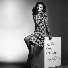 Black and white portrait of Diane von Furstenberg posing in her famous wrap dress smiling at the camera. She leans agains a short podium with the words, Feel like a woman, wear a dress! Diane Von Furstenberg are written in her handwriting