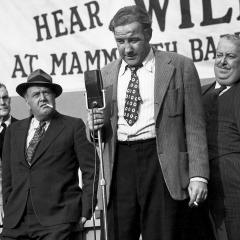 Still from the 1949 film All the King’s Men showing Broderick Crawford as Willie Stark standing on an outdoor stage making a stump, political speech.