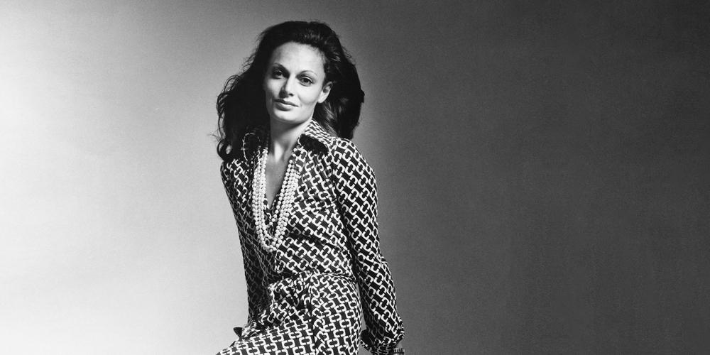 Black and white portrait of Diane von Furstenberg posing in her famous wrap dress smiling at the camera.