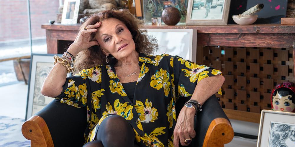 Diane von Furstenberg posing for the camera while sitting in a large armchair in her home.